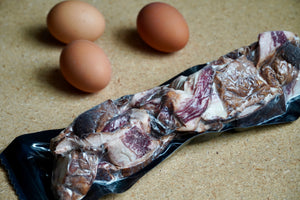 Raw, packaged Wagyu bacon ends  with three brown eggs on a beige surface