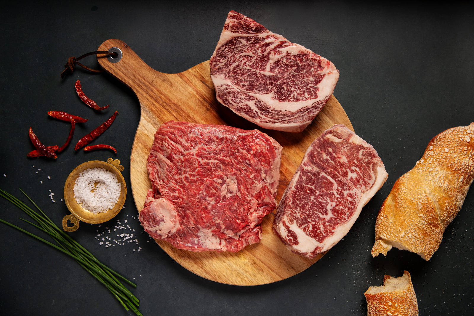 A cutting board with one ribeye, one NY Strip, and one Bavette Wagyu steak. 