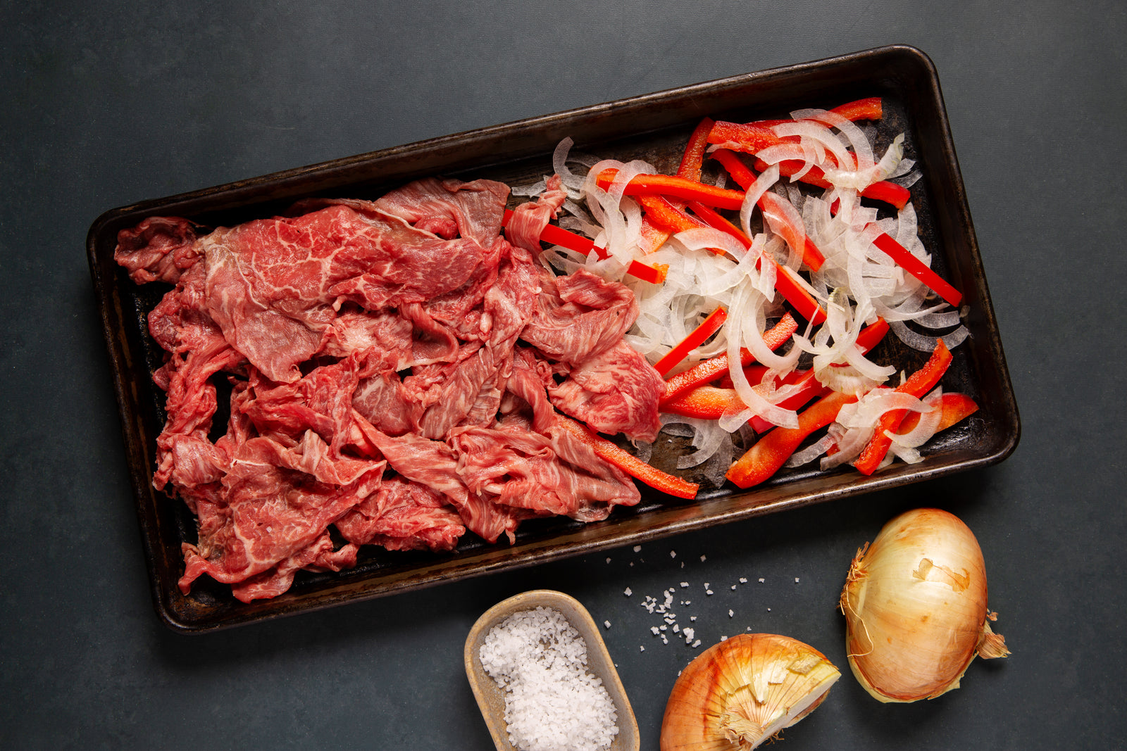 a sheet pan with shaved wagyu steak, onions, and peppers