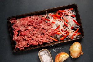 a sheet pan with shaved wagyu steak, onions, and peppers