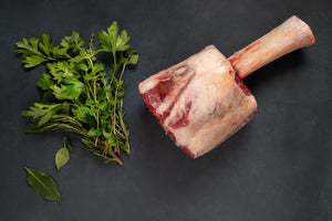 Thor's Hammer steak cut on a slate background next to a bundle of herbs.